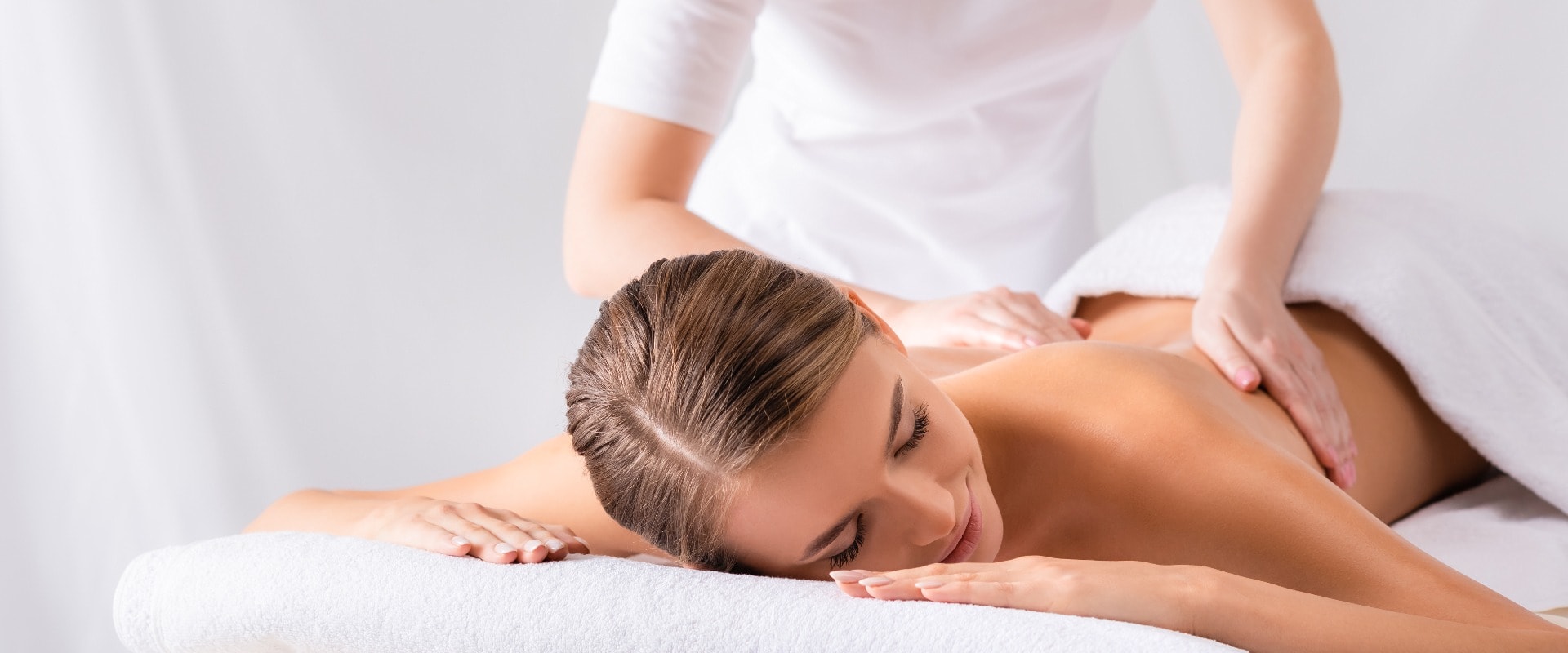 masseur massaging pleased young woman on massage table in spa salon, banner