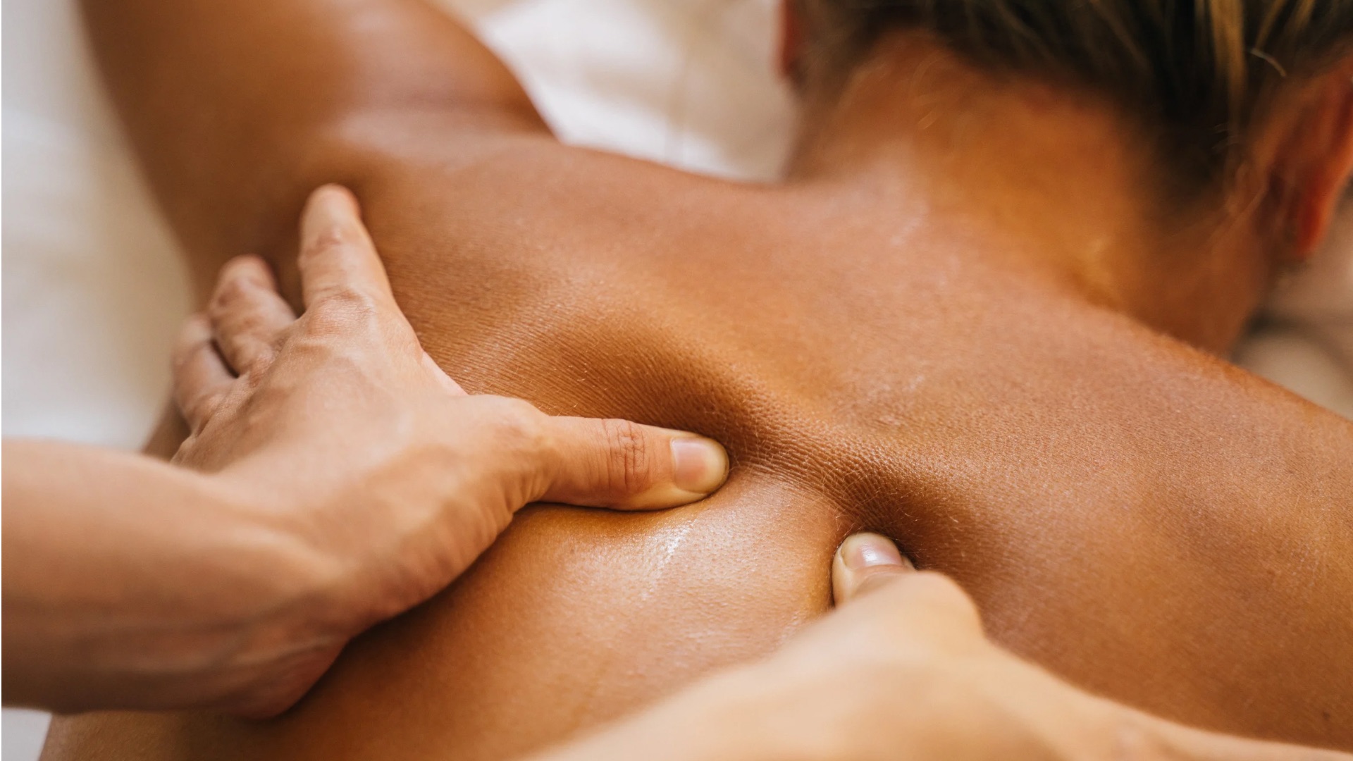 Eine Person erhält eine Massage, Hände drücken sanft auf einen braunen Rücken